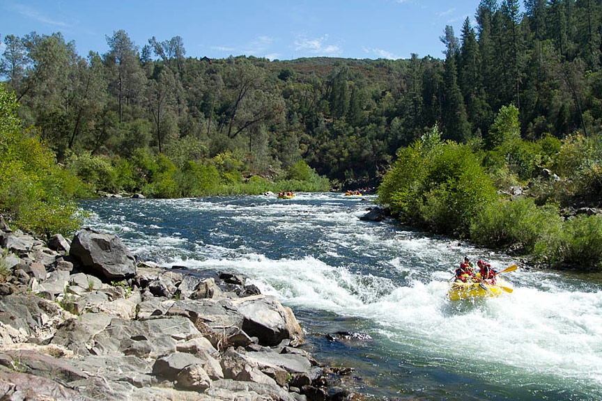 American River with white water rapids and rafters navigating through rocky terrain