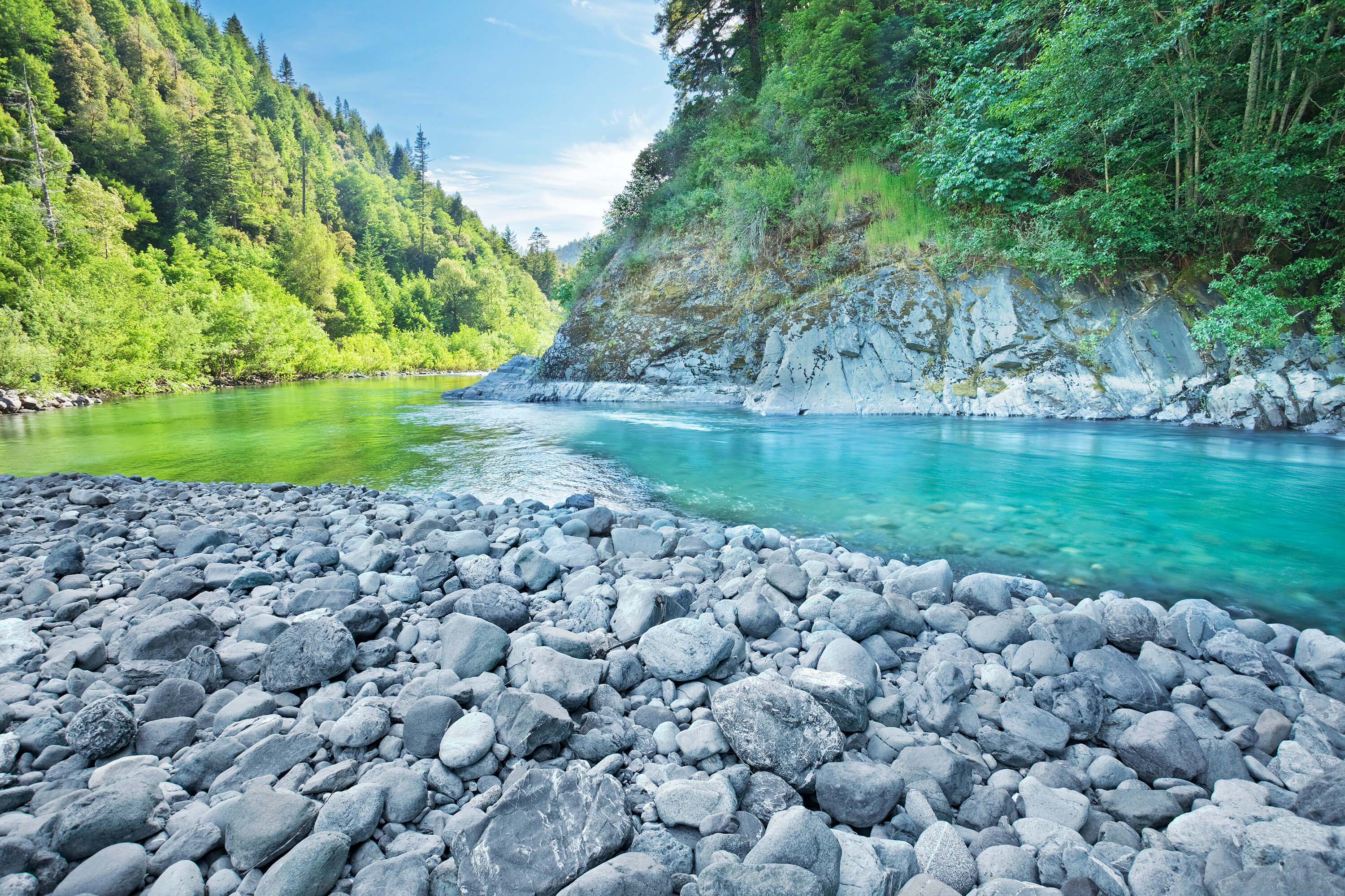 Klamath River with crystal clear turquoise water and rocky shores surrounded by forested hills